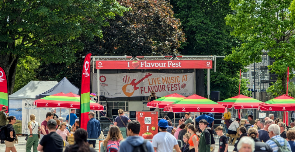 Crowds enjoy live music at an outdoor Flavour Fest stage surrounded by colourful market stalls.